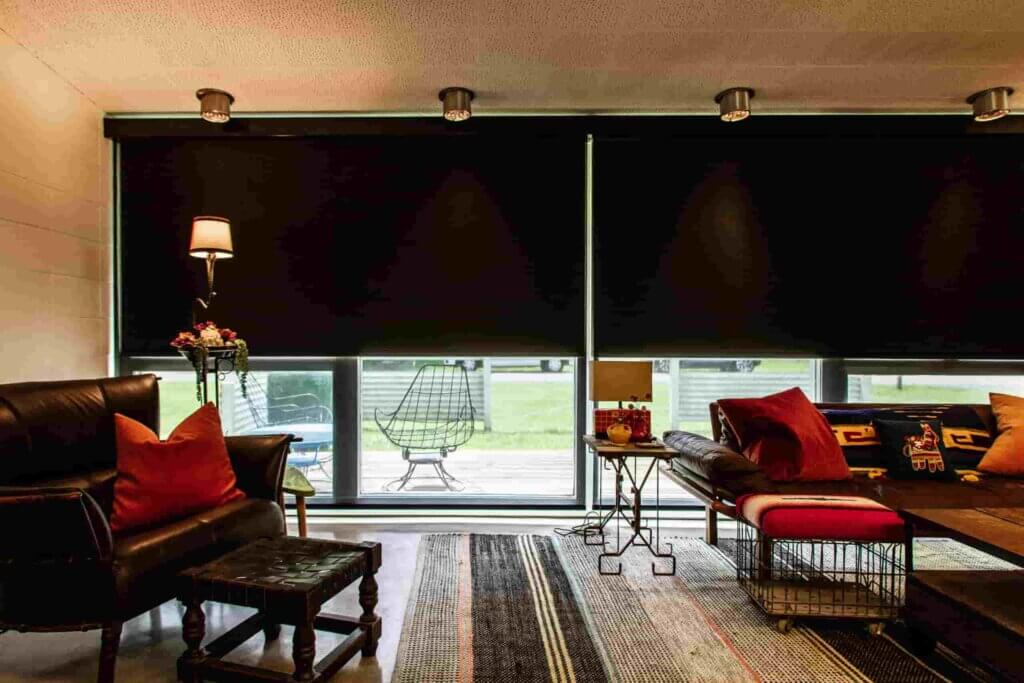 A living room with black roller shades and red pillows.