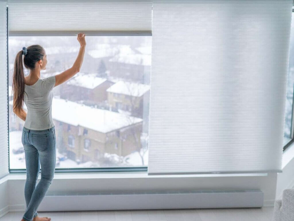 A woman standing in front of a window with her arms up.