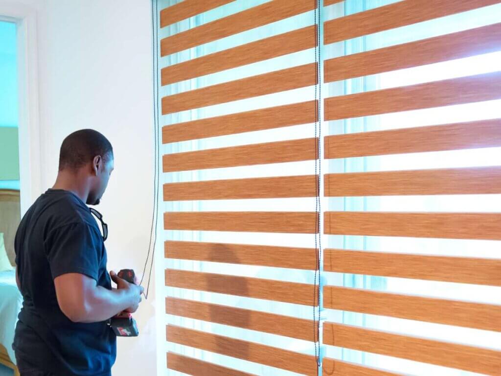 A man in blue shirt painting wooden blinds.